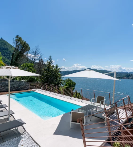 Un moderno ponte della piscina con sedie a sdraio, ombrelloni e posti a sedere si affaccia su un lago panoramico circondato da colline verdi e cielo blu, catturando l'essenza di una fotografia bed & breakfast di lusso sul Lago di Como in un ambiente soleggiato e tranquillo. Un moderno ponte della piscina con sedie a sdraio, ombrelloni e posti a sedere si affaccia su un lago panoramico circondato da colline verdi e cielo blu, catturando l'essenza di una fotografia bed & breakfast di lusso sul Lago di Como in un ambiente soleggiato e tranquillo.